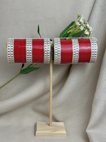 Complete red Punjabi bridal chooda set for both arms displayed on a wooden stand.