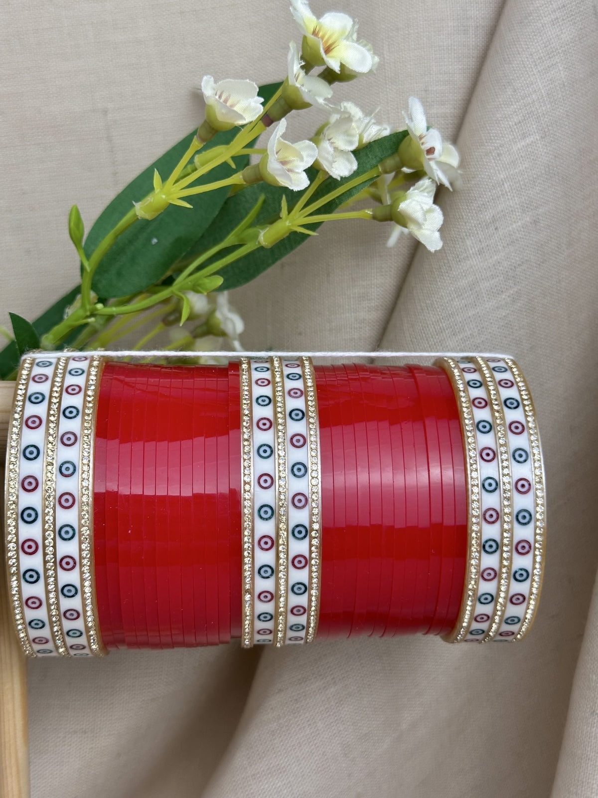 Close-up of red bridal bangles with white patterned bangles, stone borders and gold-toned detailing.