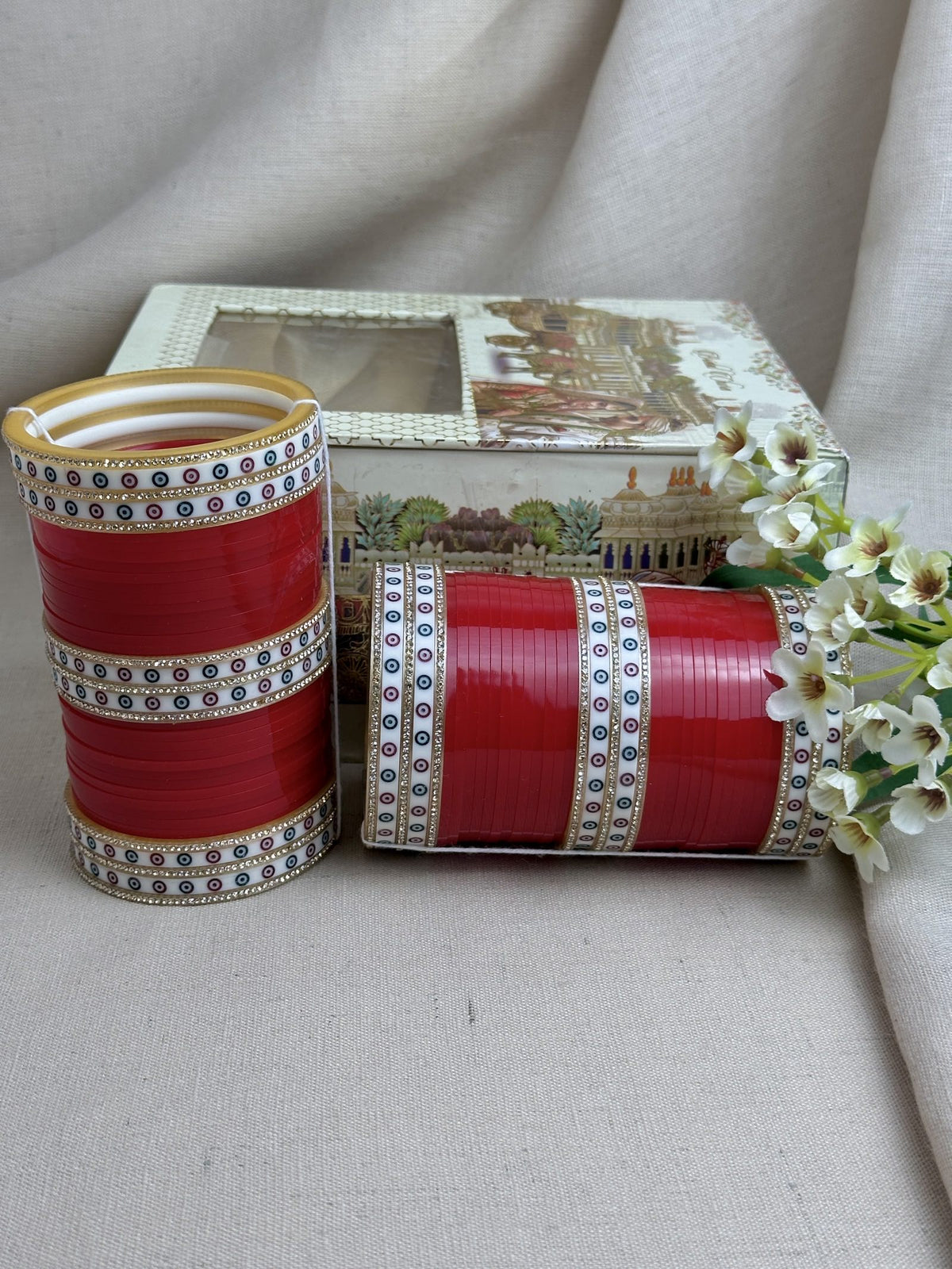 Red Punjabi bridal chooda set styled upright and horizontally beside its bridal box.