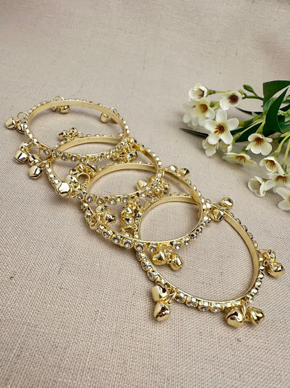 Flat lay out of gold ghungroo bangles with clear stones and hanging bell charms