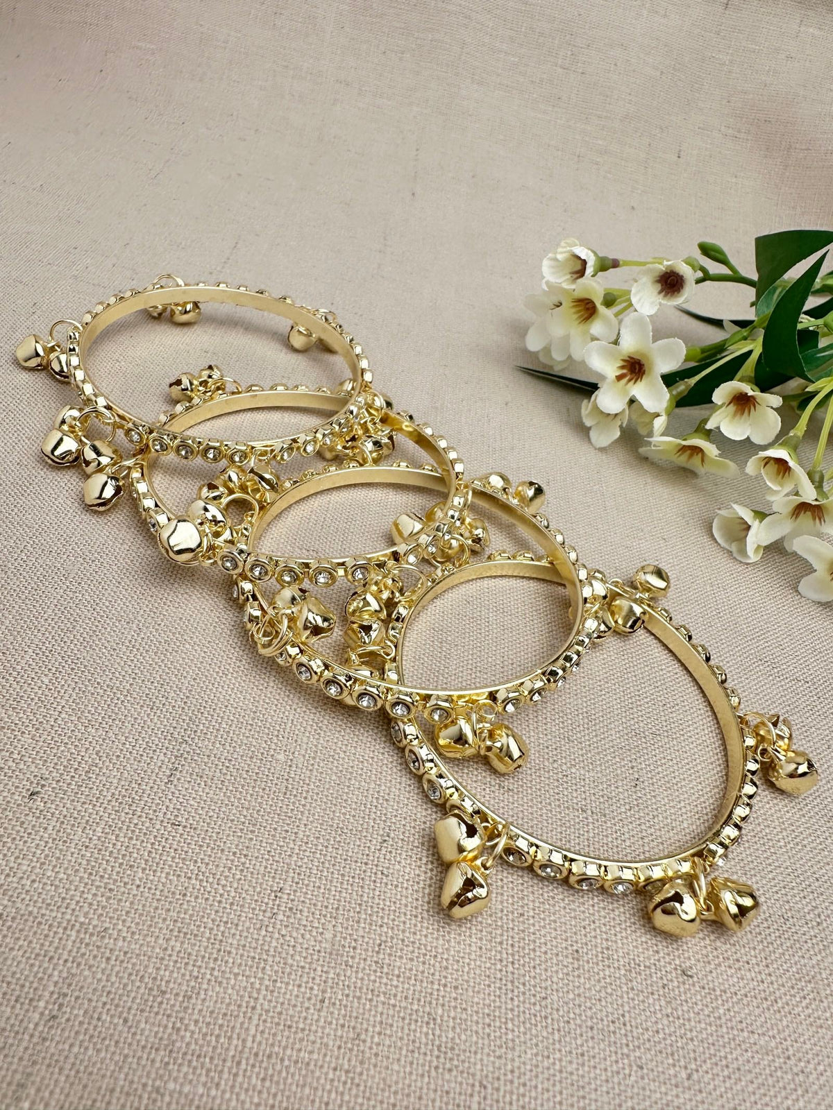 Flat lay out of gold ghungroo bangles with clear stones and hanging bell charms