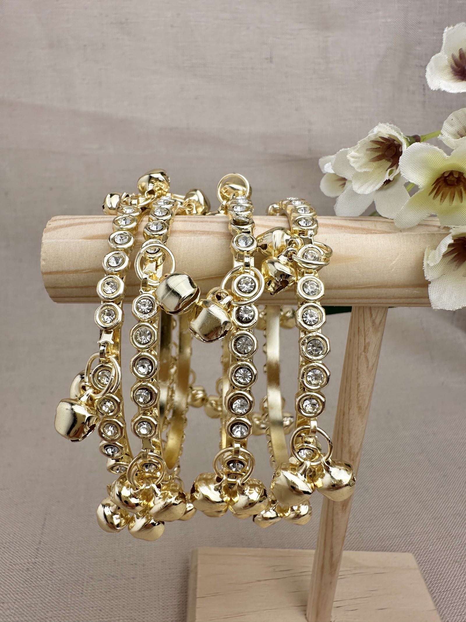 Set of four gold tone ghungroo bangles with clear decorative stones