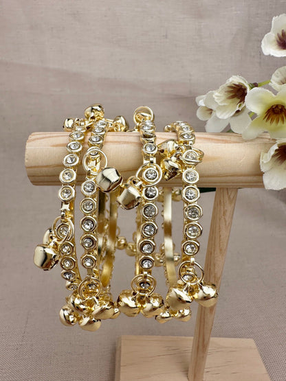 Set of four gold tone ghungroo bangles with clear decorative stones
