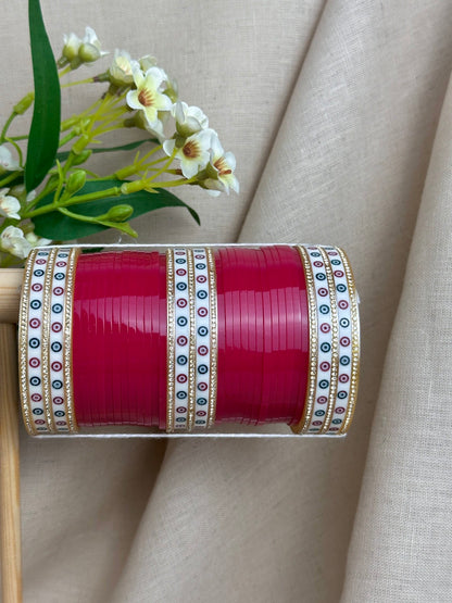 Close-up of hot pink bridal bangles with white patterned bangles, stone borders and gold-toned detailing.
