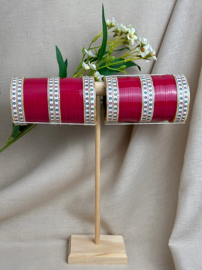 Complete hot pink Punjabi bridal chooda set for both arms displayed on a wooden stand.