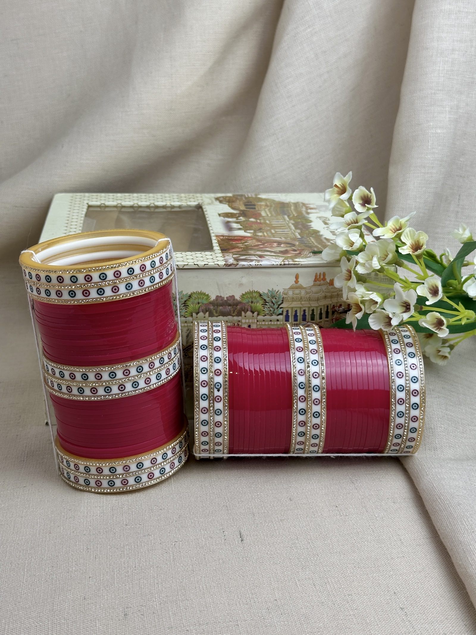 Hot pink Punjabi bridal chooda set styled upright and horizontally beside its bridal box.