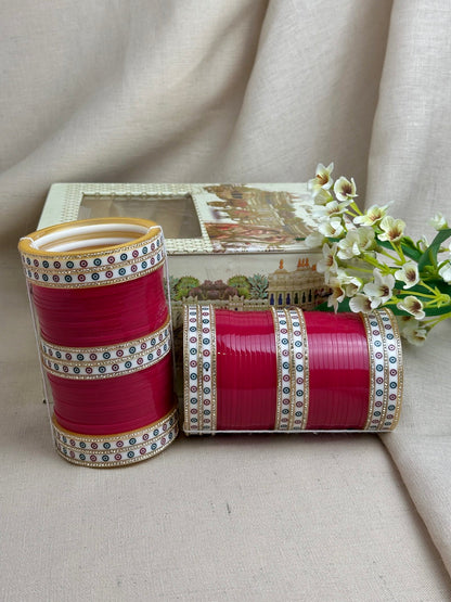 Hot pink Punjabi bridal chooda set styled upright and horizontally beside its bridal box.