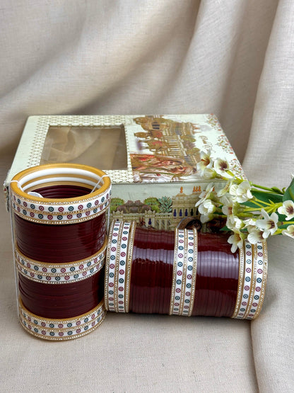 Maroon Punjabi bridal chooda set styled upright and horizontally beside its bridal box.