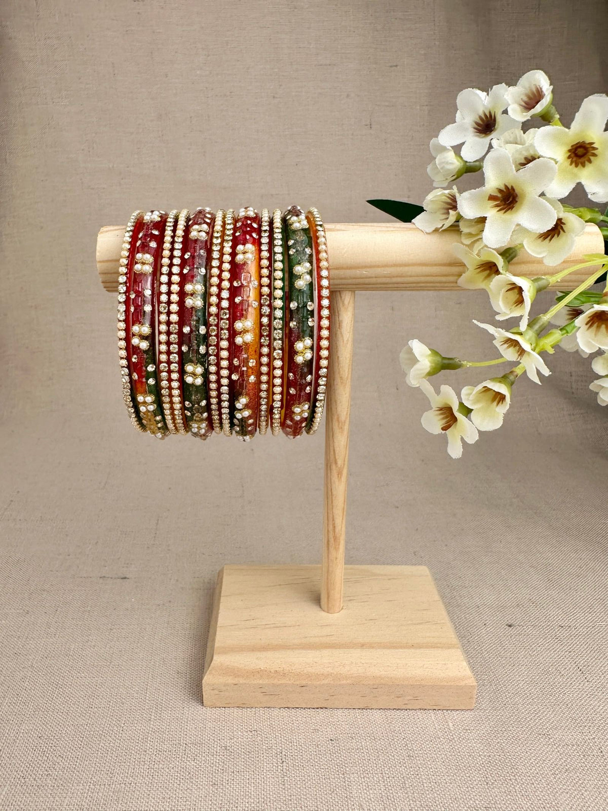 Noor Dark Multi glass bangles set of 12 featuring rich red and green tones with pearl embellishments and gold-tone stone-studded bangles.