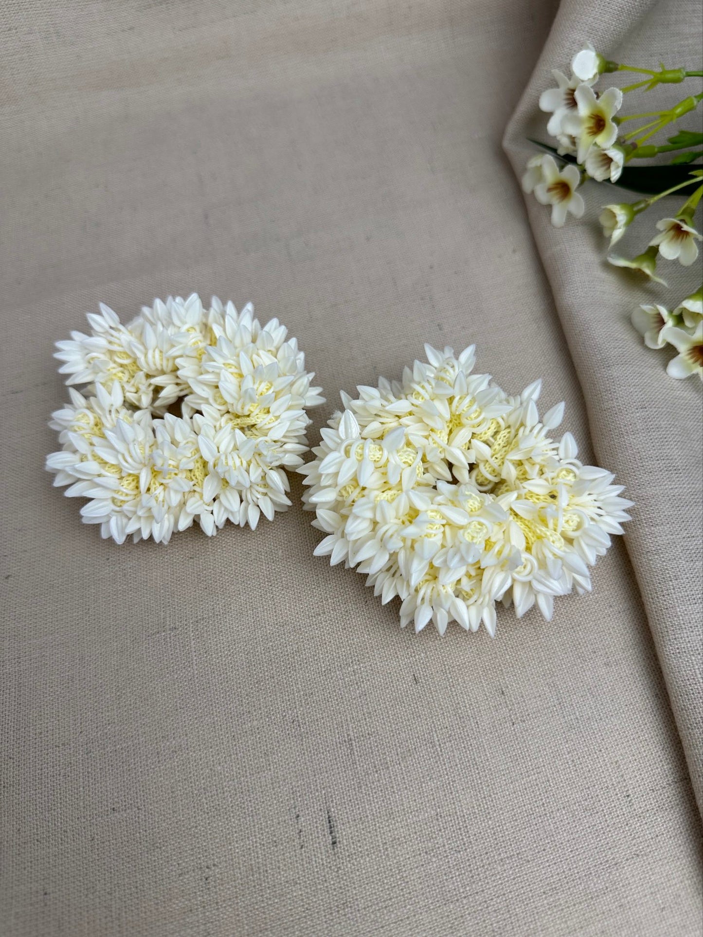Pair of off-white reusable artificial gajras displayed on cream fabric.