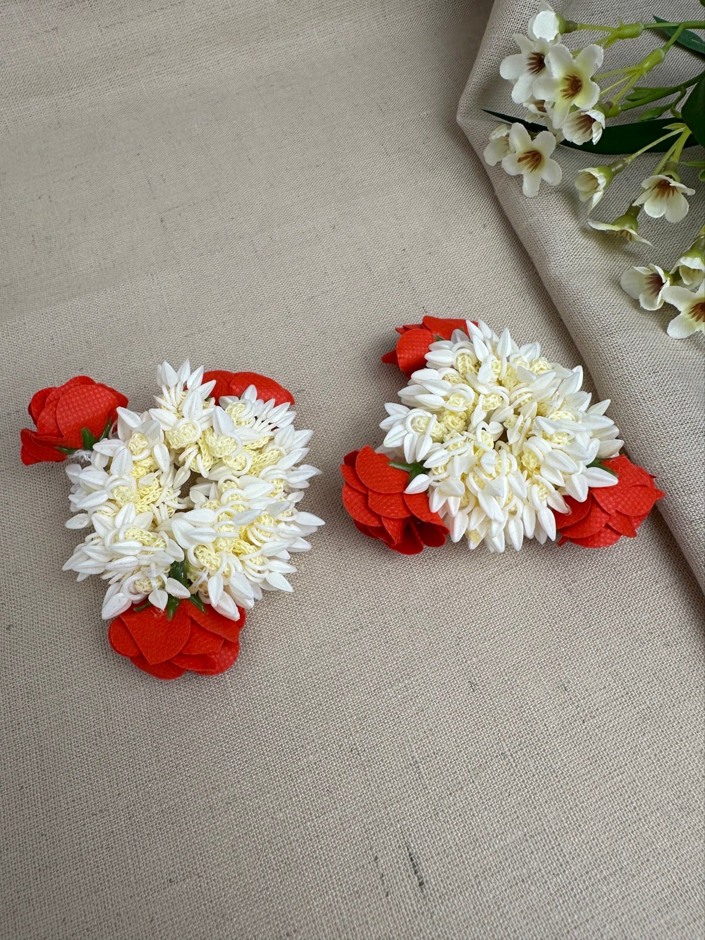 Pair of red and off-white reusable artificial gajras displayed on cream fabric.