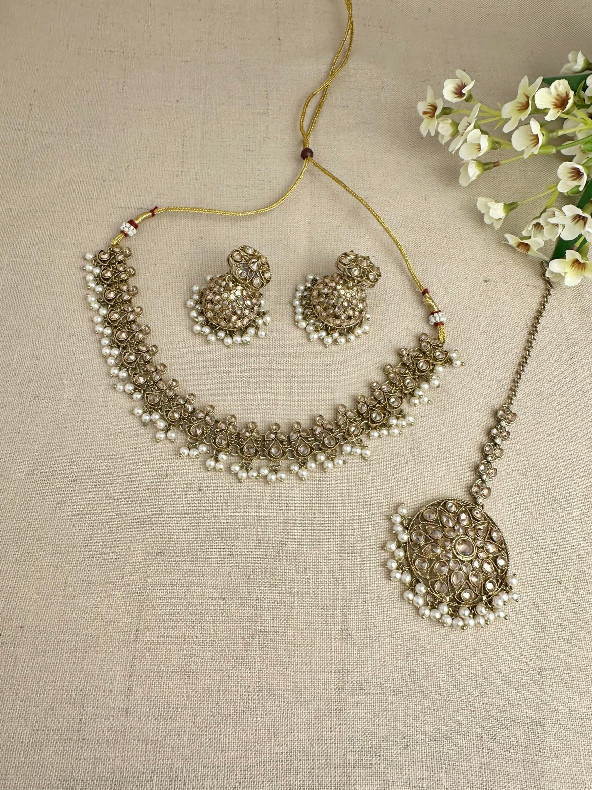 Flat-lay view of Saanjh champagne necklace, jhumki and tikka set